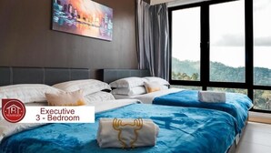Habitación de hotel tipo ejecutivo de tres dormitorios con un amplio ventanal que ofrece vistas al paisaje.