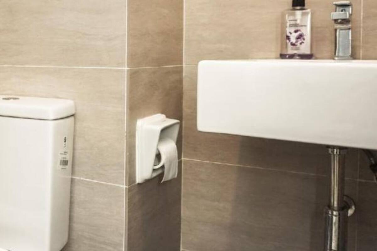 A bathroom with a toilet, a hand dryer, a paper towel dispenser, and a sink with a faucet.