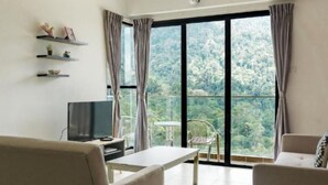 Un salón con sofá, televisor, mesa y vistas a un bosque a través de amplios ventanales.