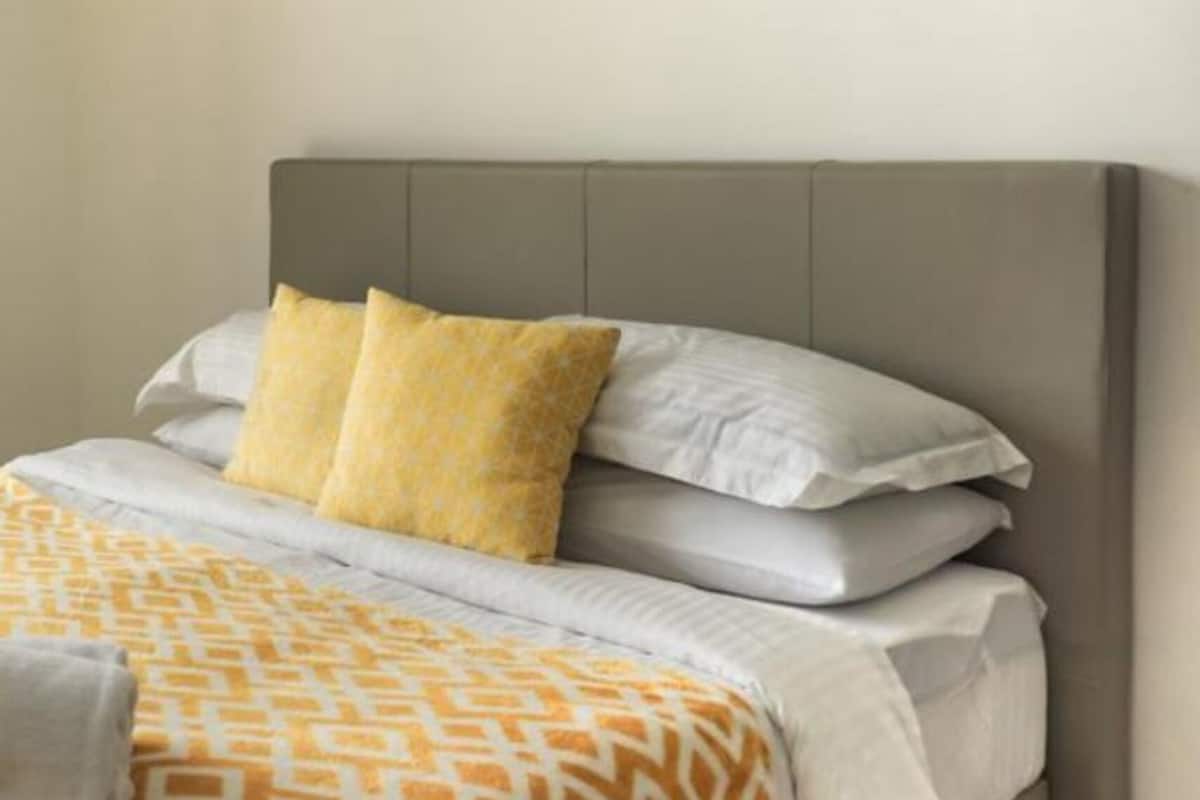A bed with a grey headboard, white and yellow pillows, and a patterned bedspread.