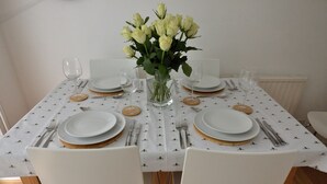 A dining table set with white plates, gold rims, and silver cutlery. A clear glass vase with white flowers is centered on the table.