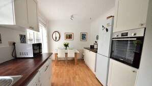 A compact kitchen with a microwave, oven, and washing machine. There is a dining table with chairs and a vase with flowers.