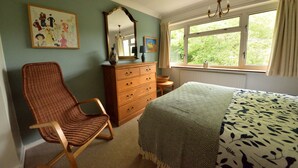 A bedroom with a bed, dresser, chair, and a window with a view of greenery.