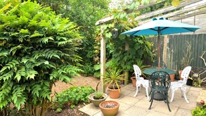 A patio with a table and chairs, surrounded by potted plants and a wooden pergola.