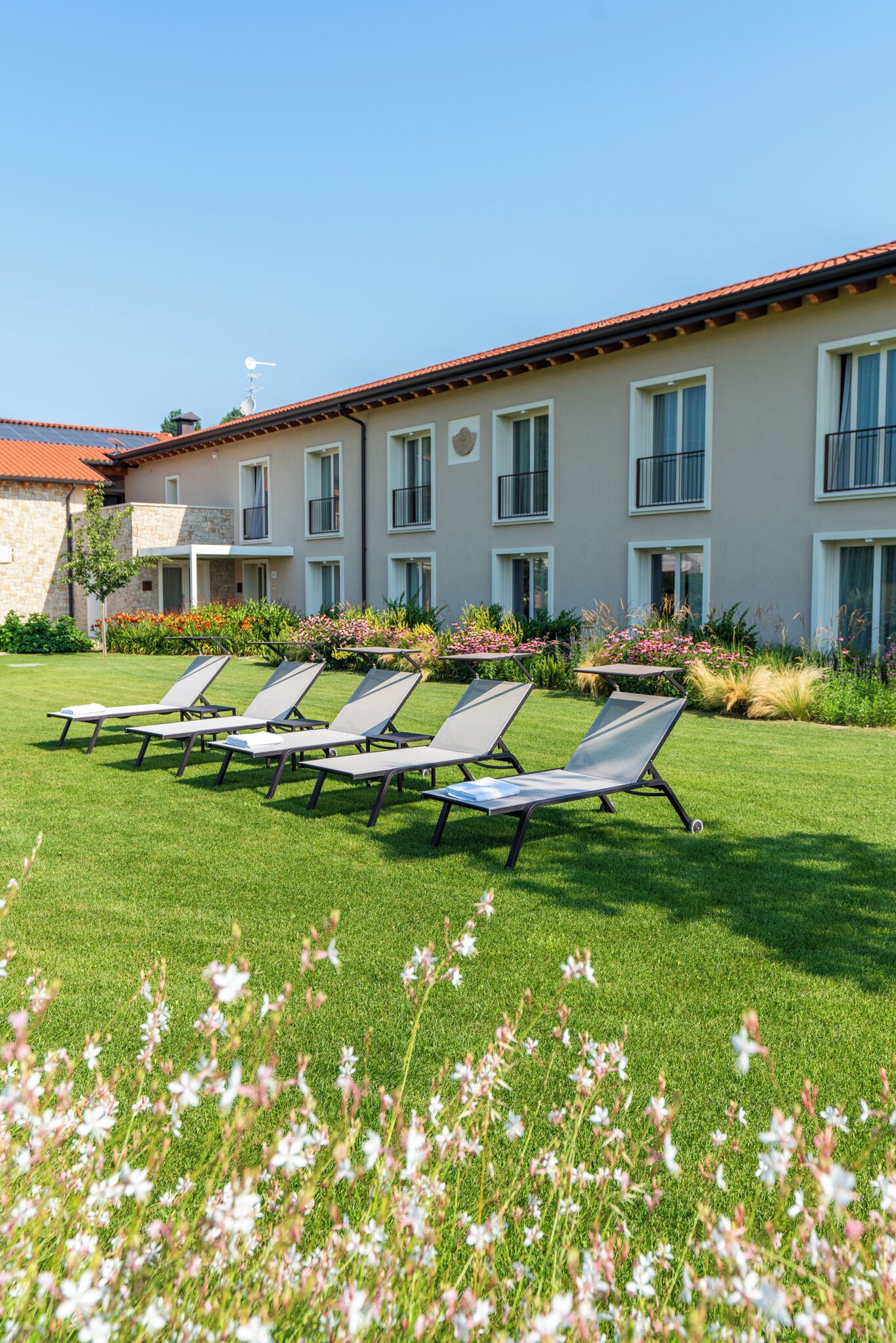 A building with a red-tiled roof, multiple windows, and a well-maintained lawn with sun loungers.