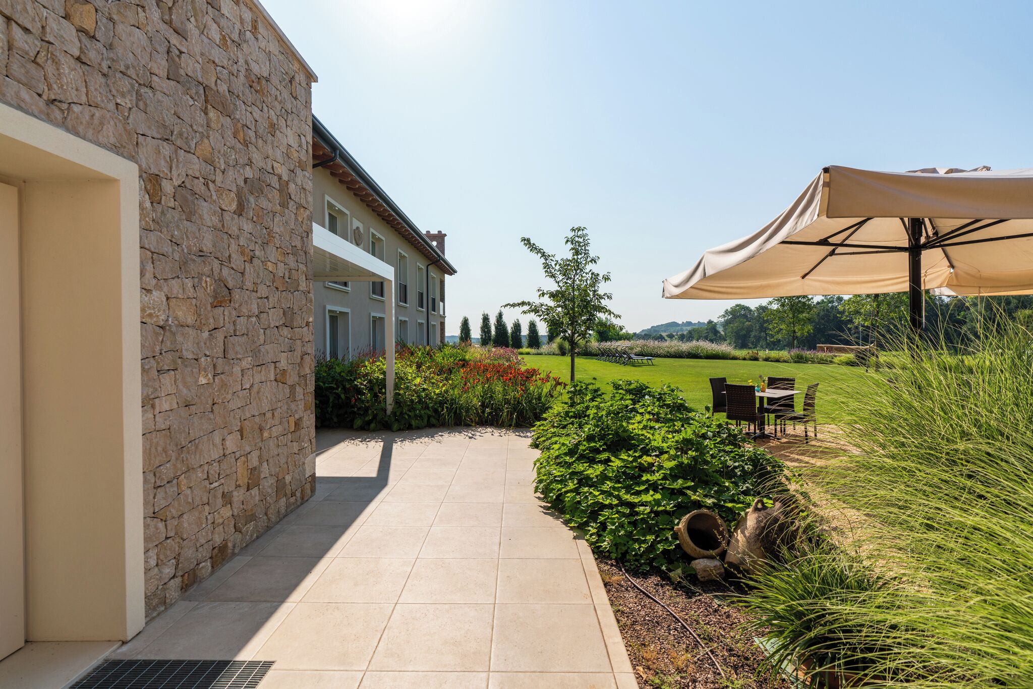 Un edificio de piedra con patio, mesas al aire libre y vista a un campo verde.