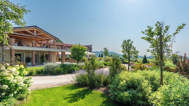 Een modern huis met een overdekt terras, een weelderige tuin en een helder uitzicht op het landschap.