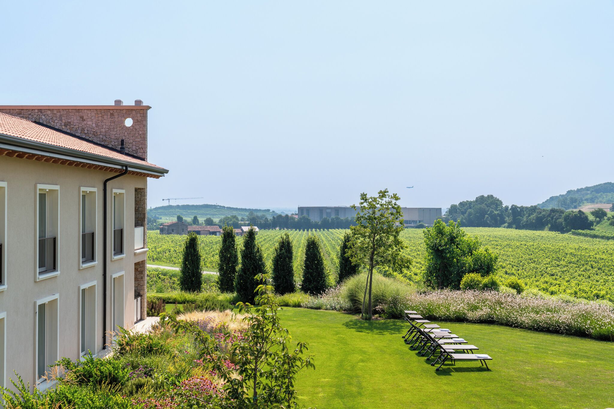 A building with a stone facade and a tiled roof, a well-maintained lawn, and a row of outdoor tables and chairs.