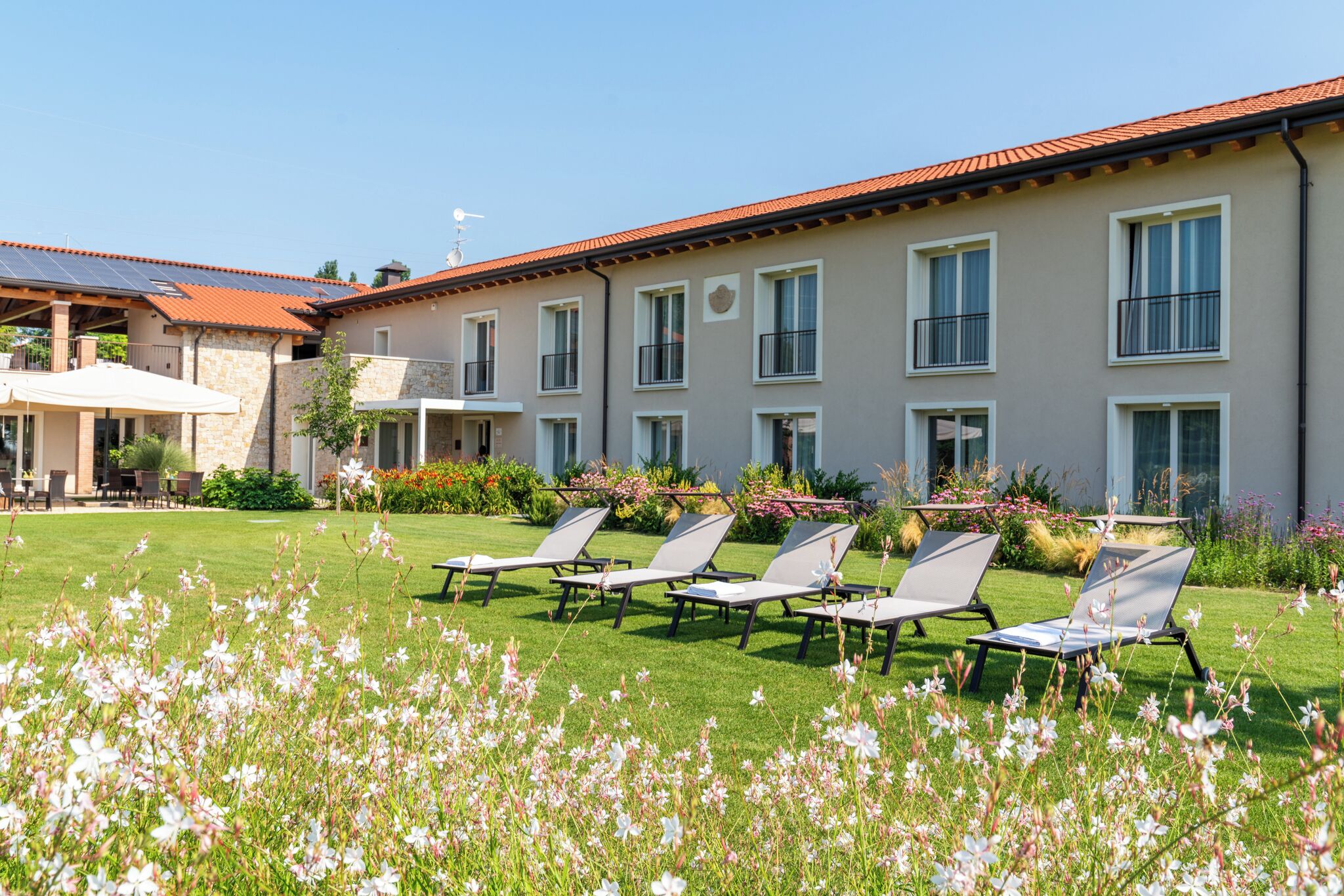 A building with multiple windows, a red-tiled roof, and a lawn with sun loungers.