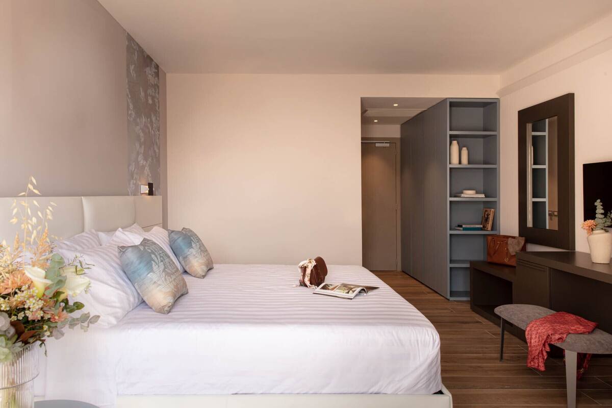 Un dormitorio moderno con una cama grande, una mesita de noche, un banco y una unidad de estanterías empotradas.