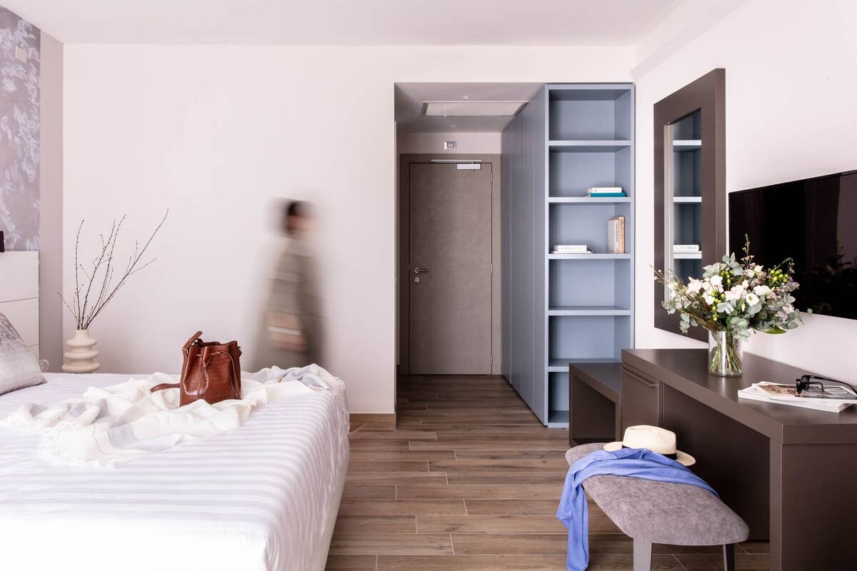 Un dormitorio moderno con cama, una mesita de noche con un florero, un banco y un armario con estantes abiertos.