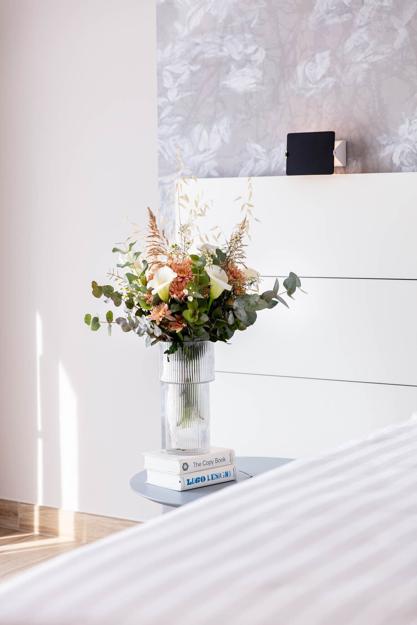 Une pièce moderne avec un vase en verre transparent contenant une composition florale, posé sur une console blanche.