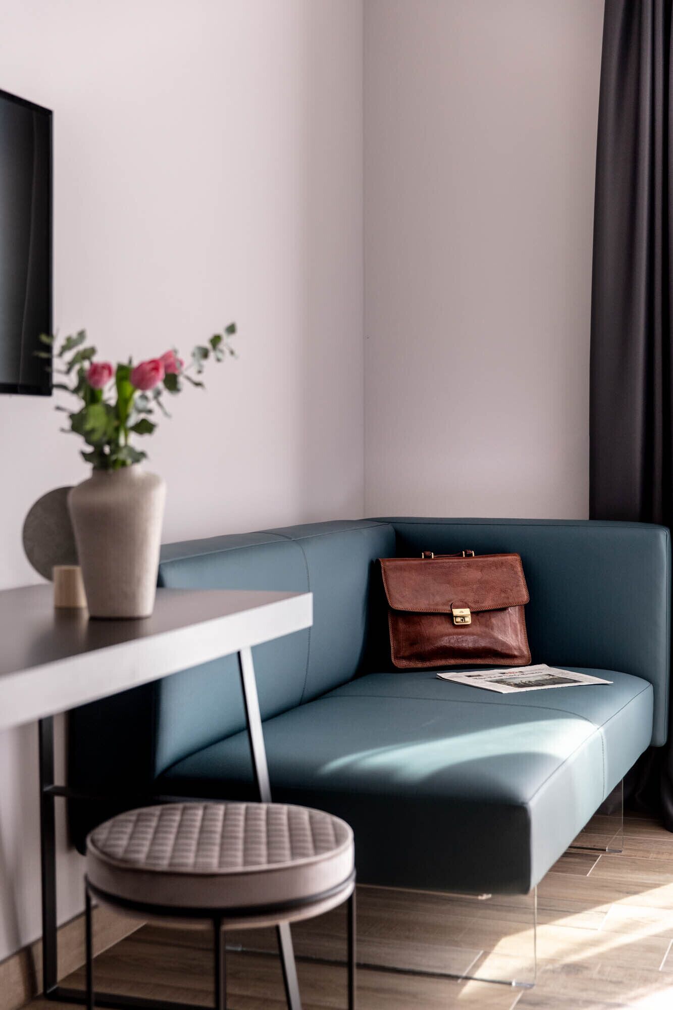 A modern living space with a blue sofa, a small round ottoman, a white table, and a vase with flowers.