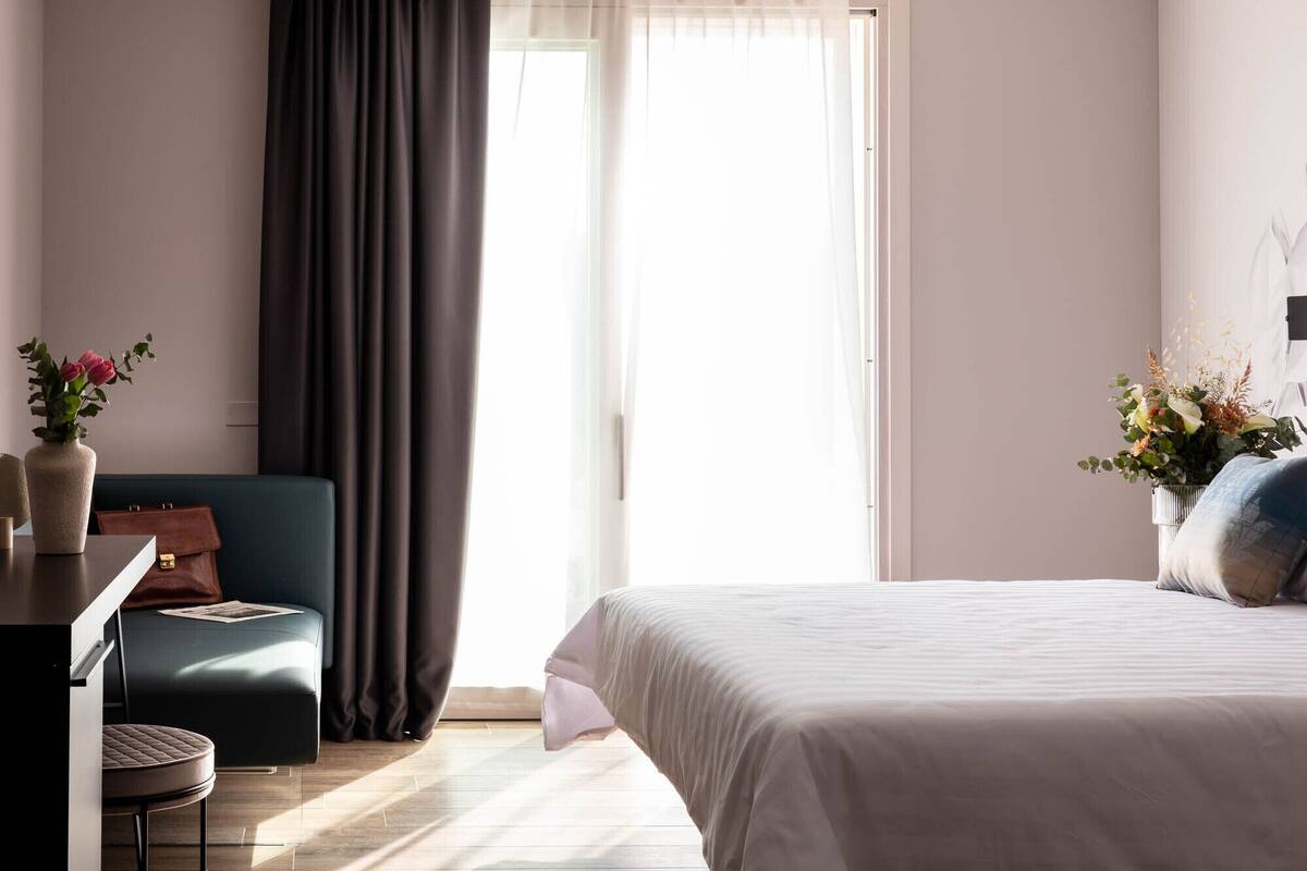 Habitación de hotel moderna con cama, escritorio, silla y un ventanal con cortinas.
