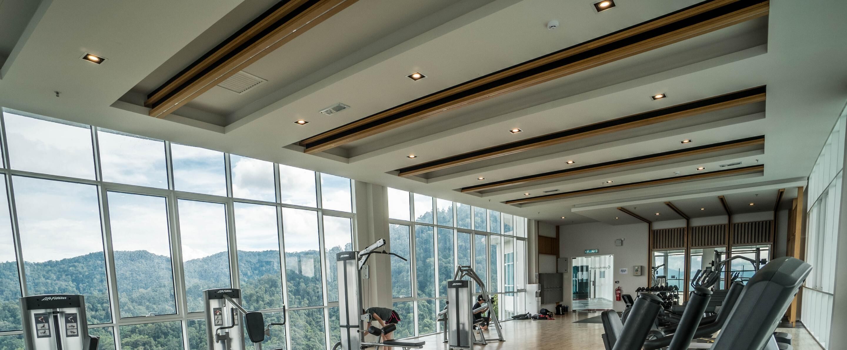 Une salle de sport dotée de grandes fenêtres, d’équipements d’exercice et offrant une vue sur un paysage montagneux.