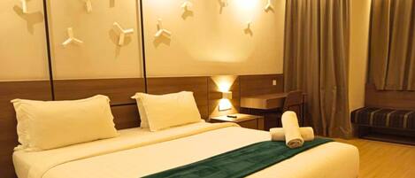 A hotel room with a neatly made bed, a bedside lamp, a small table, and a bench.