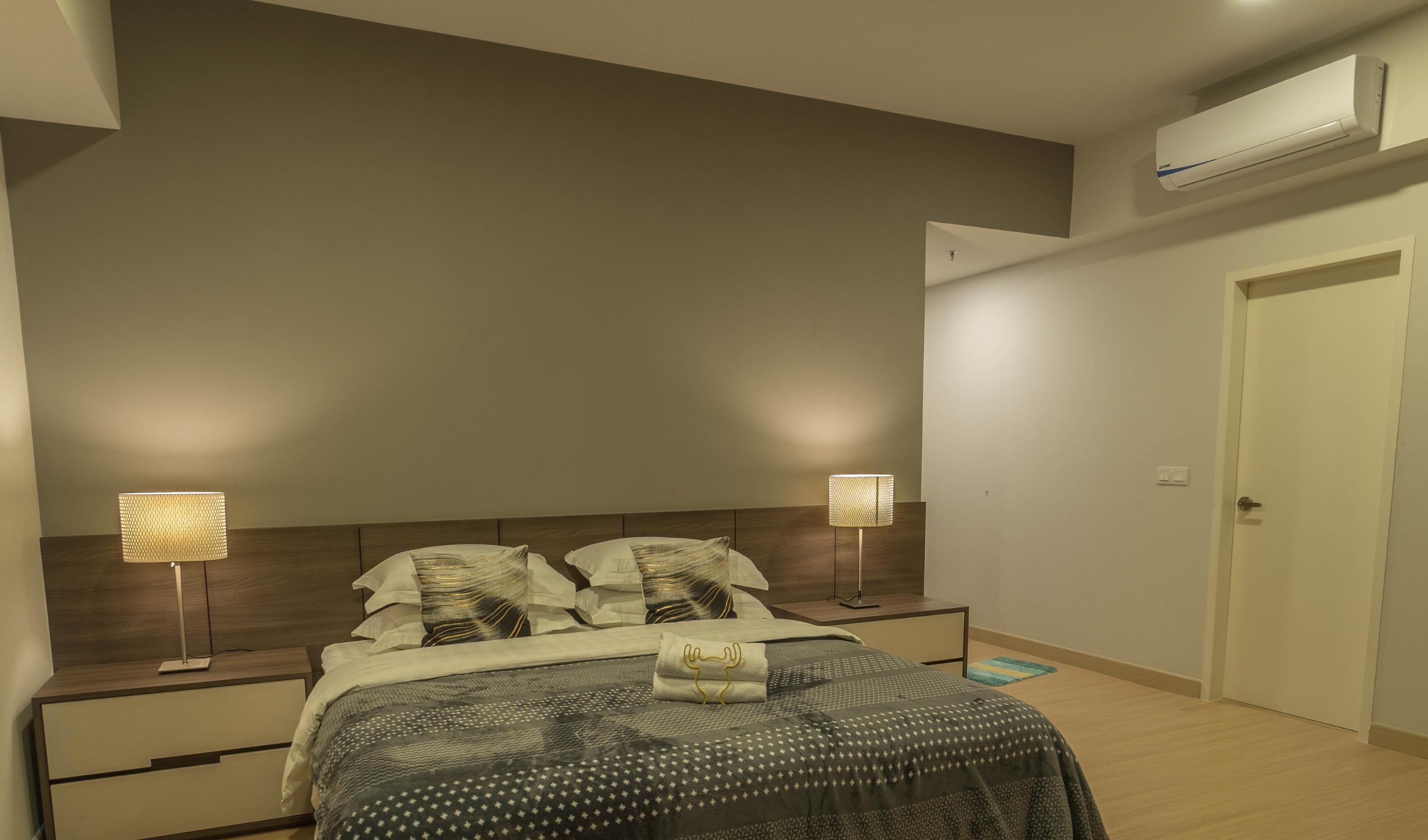 Un dormitorio con cama, lámparas de noche, mesita de noche, una puerta y un equipo de aire acondicionado.