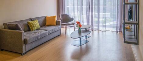 A modern living room with a grey sofa, two cushions, a small round table with a vase of flowers, and a chair.