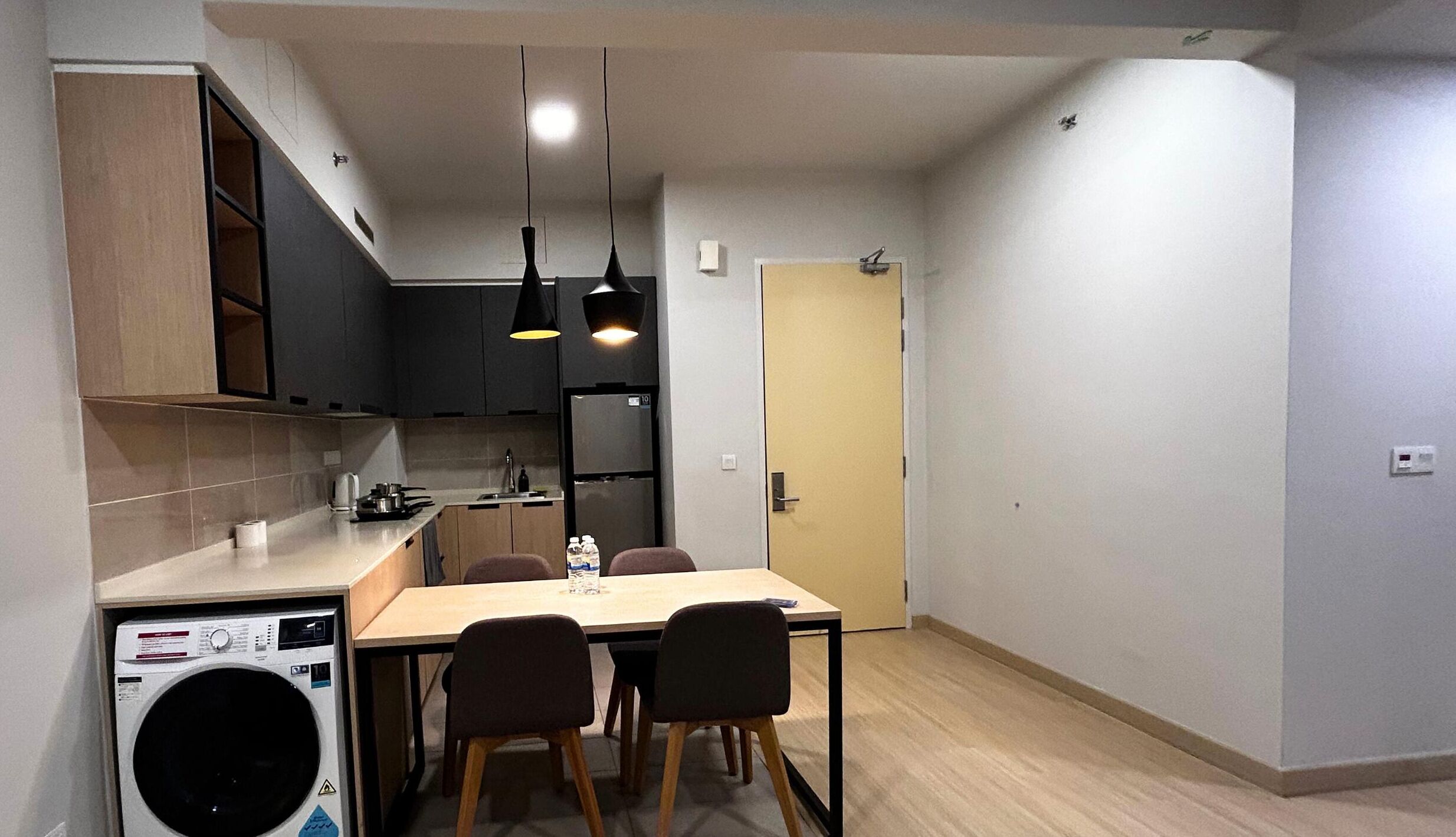 A compact kitchen with a washing machine, a dining table with chairs, and pendant lights.