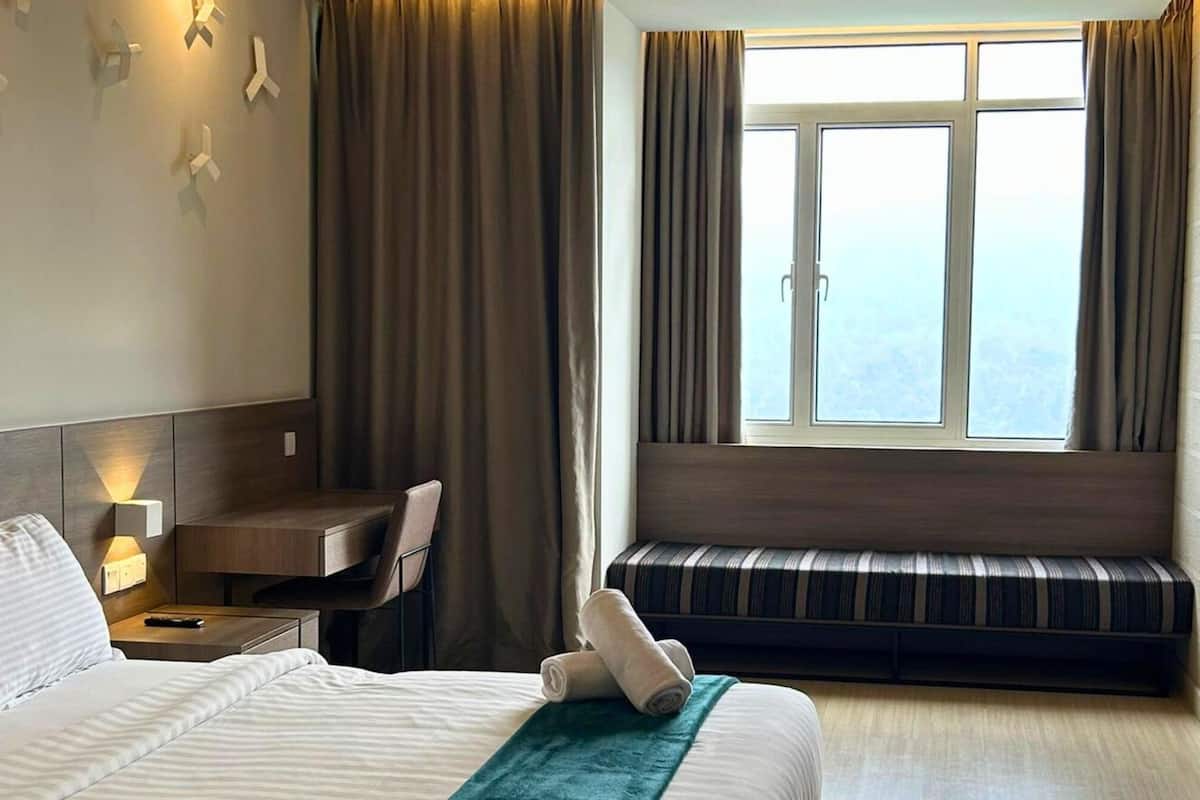 A hotel room with a bed, a desk, a bench, and a large window with curtains.