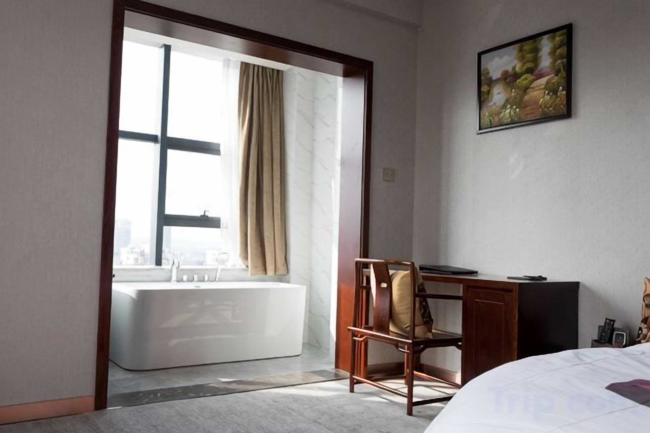 Ein Hotelzimmer mit großem Fenster, einer Badewanne, einem Schreibtisch und einem Bett.