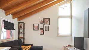Ein modernes Wohnzimmer mit schräg verlaufender Decke, einem schwarzen Sofa, einem kleinen Tisch und einem Fernseher.