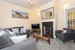 A living room with a sofa set, a coffee table, a flat-screen TV, a fireplace, and a large mirror.