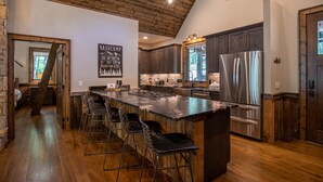 Una cocina moderna con una isla grande, taburetes de bar, electrodomésticos de acero inoxidable y un cartel de pizarra.