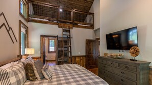 Un dormitorio con una cama grande, un aparador de madera, un televisor y una zona superior con una escalera.