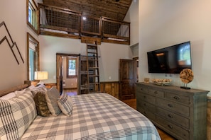 Un dormitorio con una cama grande, un aparador de madera, un televisor y una zona superior con una escalera.