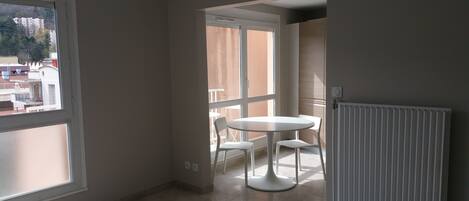 Una habitación con un ventanal grande, una mesa redonda blanca con sillas y un radiador.