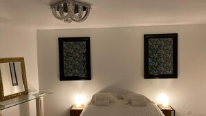 A bedroom with a bed, two bedside tables with lamps, a mirror, and two framed floral artworks on the wall.