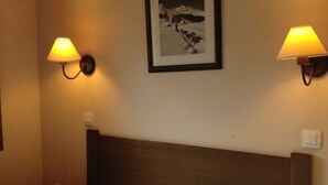 Ett hotellrum med en säng, två vägglampor och en inramad tavla på väggen.