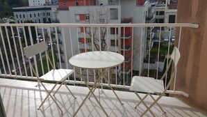 Un balcón con una mesa blanca y dos sillas blancas, con vistas a una zona residencial con edificios de varios pisos.