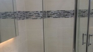 Un baño moderno con cabina de ducha de vidrio, un lavabo blanco y un salpicadero de azulejos.