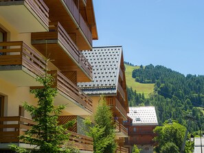 Ein mehrstöckiges Gebäude mit hölzernen Balkonen, einem geneigten Dach und Blick auf einen grünen Hügel.