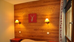Ein Schlafzimmer mit Holzkopfteil, zwei Nachttischlampen, einem Bett mit gemustertem Überwurf und einem roten Kunstwerk darüber.