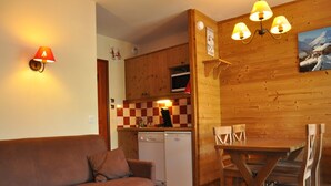 Ein gemütliches Wohnzimmer mit einer Couch und einem Couchtisch, ein Holzespeisetisch mit Stühlen, eine Küchenzeile mit einer Mikrowelle und einem Geschirrspüler sowie Holzwände mit einer karierten Spritzschutzleiste.