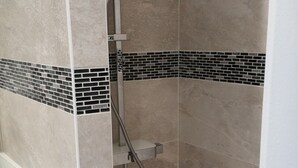 Zona de ducha con paredes de azulejos, cabezal de ducha metálico y lavamanos blanco.
