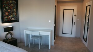 Un dormitorio con cama, escritorio, silla, lámpara y puerta.