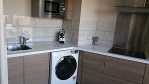 Una cocina compacta con lavadora integrada, un microondas y una campana extractora de acero inoxidable.