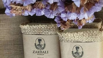Twee verpakkingen Zarbali Ayvalik Hamam olijfoliënzeep, elk 150 gram, op een gestructureerd oppervlak, met een bloemstuk erboven.