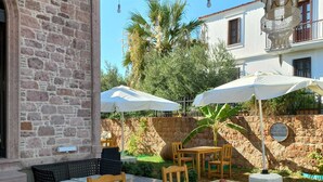 An outdoor patio with a wooden table and chairs, surrounded by stone walls and palm trees. - Zarbalı Cunda (Ayvalik)