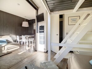 A modern living room with a sofa, dining table, and chairs, a staircase, and a view of the outdoors. - Renovated 2-room apartment, balcony, near slopes (Les Menuires)