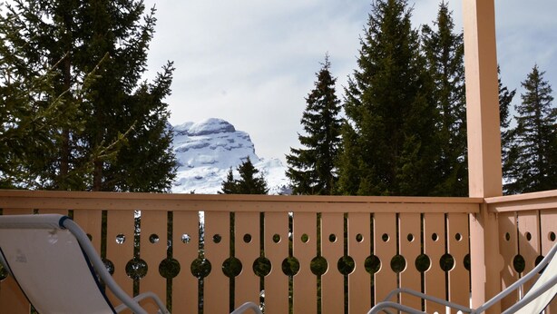 A balcony with two white lounge chairs, a wooden fence, and a mountain in the background. - Spacious Duplex 3BR - Sleeps 6/8 - Balcony (Flaine)
