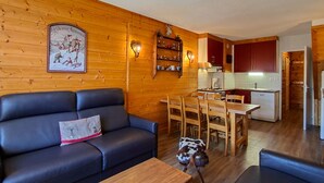 A cozy cabin interior with a wooden wall, a sofa, a dining table, and a kitchen area. - Spacious Duplex 3BR - Sleeps 6/8 - Balcony (Flaine)