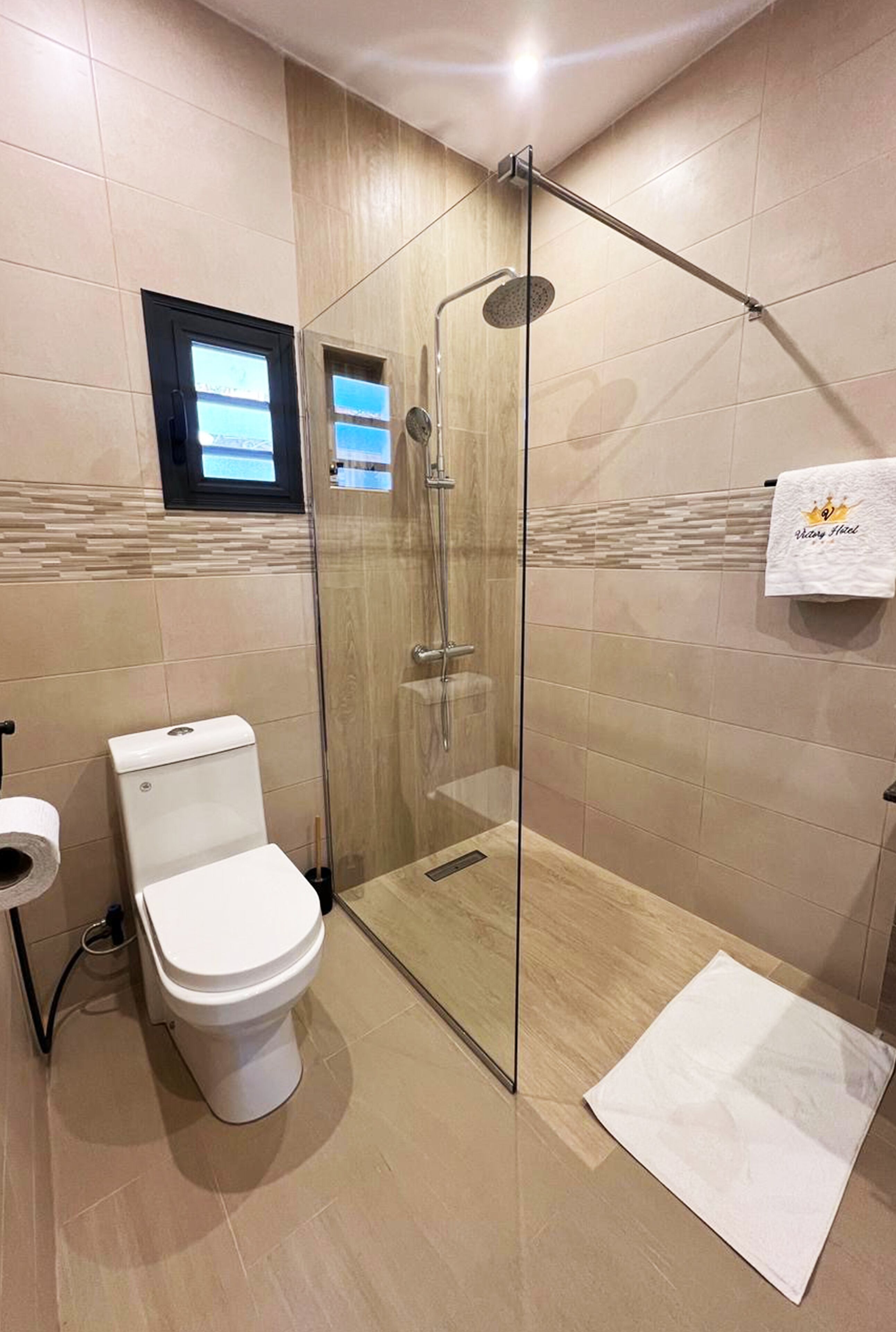 A modern bathroom with a glass-enclosed shower, a toilet, and a towel rack with a hotel logo.