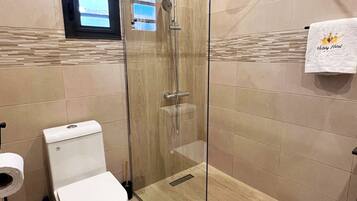 A modern bathroom with a glass-enclosed shower, a toilet, and a towel rack with a hotel logo.