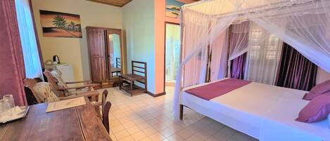 A bedroom with a bed under a canopy, a wooden desk with chairs, a mirror, and a painting on the wall.