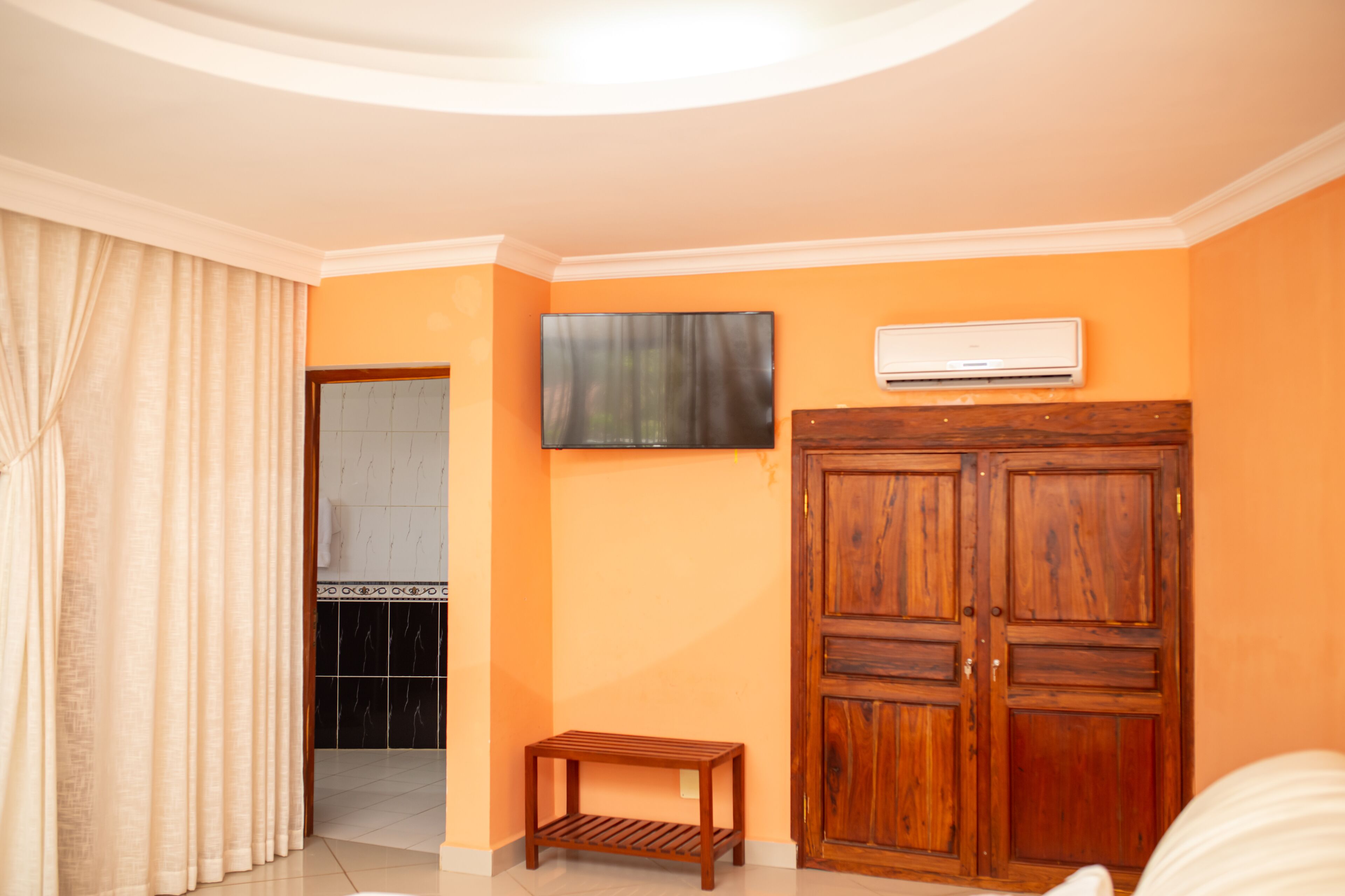 A room with a wooden wardrobe, a small wooden stool, and an air conditioning unit on the wall.